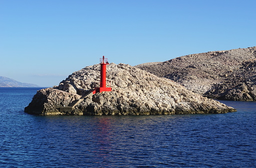 Small red lighthouse on the small picturesque stony island near the coast