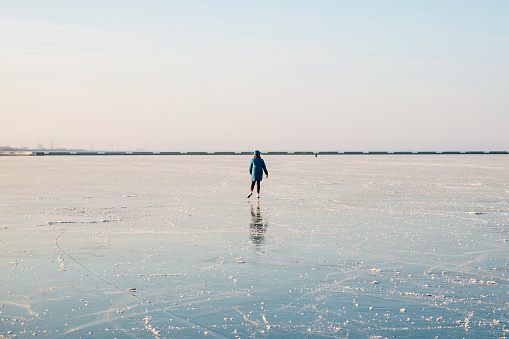 A young woman is skating on the ice of a frozen lake. Sunny day, atmosphere of fun winter activities. Minimalist photo