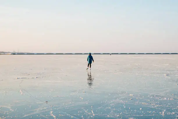 Photo of A young woman is skating on the ice of a frozen lake. Sunny day, atmosphere of fun winter activities. Minimalist photo.