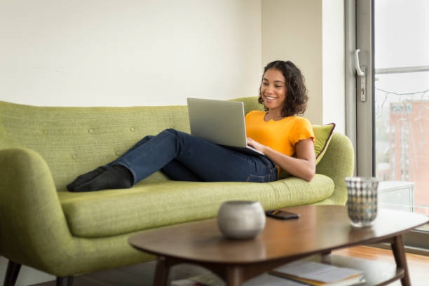 istock Happy young woman at home on sofa using a laptop 1296381688