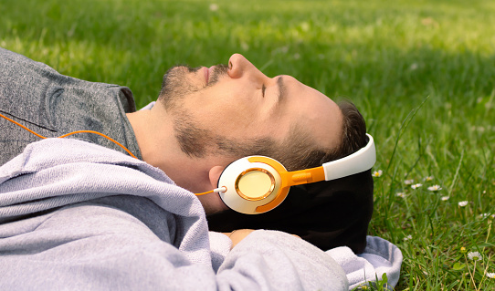 Carefree man enjoying in music over headphones and relaxing on grass in nature.