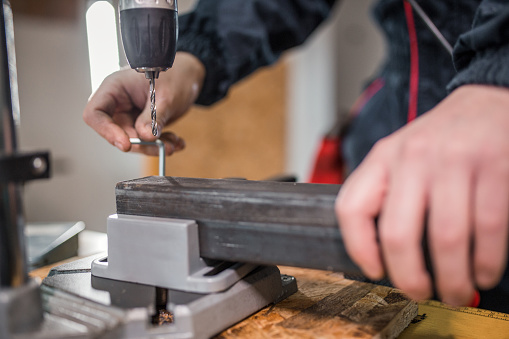 Young metal worker drilling steel pipe using machine drill in metal workshop