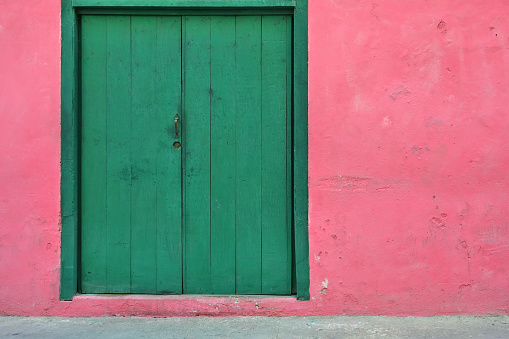 Front view of pink colored, run-down building facade with vibrant green wooden door in Havana, Habana, Cuba