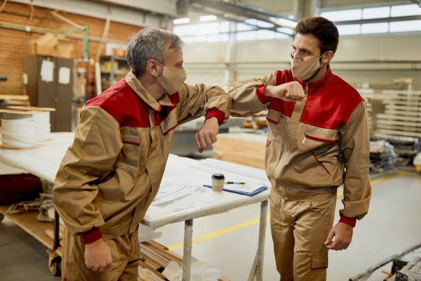 happy workers with face masks greeting with elbows at carpentry workshop. - manual worker handshake industry warehouse imagens e fotografias de stock