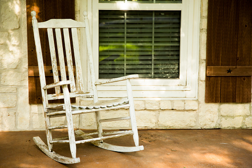 White wooded rocking chair sitting on front porch of home in rural area.