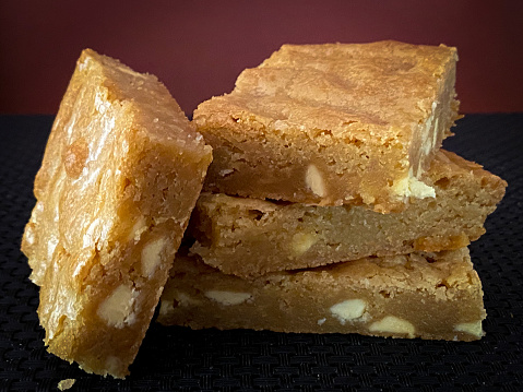 Horizontal image of a stack of blondies with white chocolate chips on a black surface