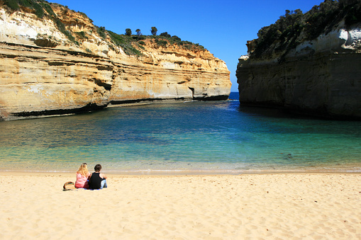 Victoria, Australia - March 8, 2012: Young couple relaxing along sand beach. Loch Ard Gorge, Port Campbell National Park on Great Ocean Road in Australia.