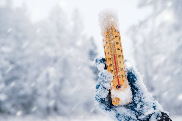 Human hand holding a thermometer with the low temperature against winter nature background with snowfall. stock photo