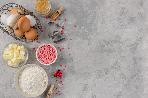 Ingredients for cooking cookies for Valentine's Day, flour, butter, eggs, sugar, chocolate and sugar hearts on a gray concrete background. Valentine's Day background. Copy space