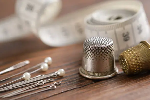 Sewing items - thimbles, including pins, measuring tape on background.