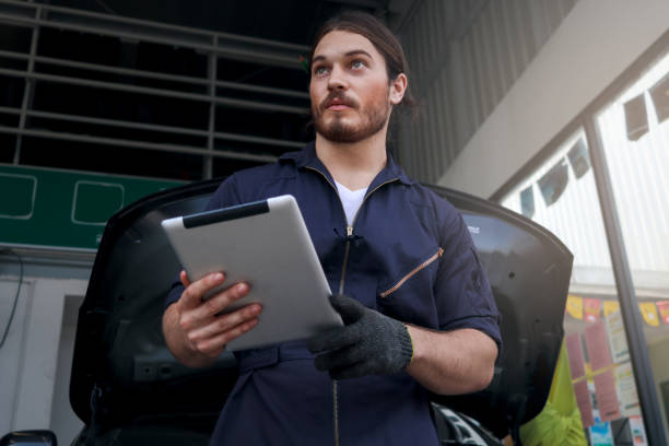 istock Auto mechanic holding digital tablet and working at garage, car service technician checking and repairing customer car at automobile service center, vehicle repair service shop concept. 1296404349