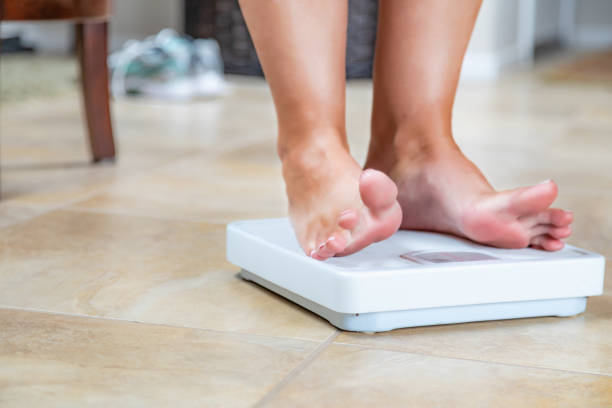 istock Woman Standing on Scale At Home Reluctantly Viewing Weight 1296405286