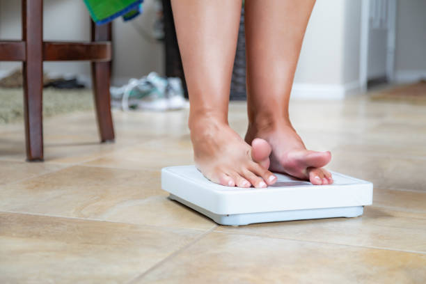 istock Woman Standing on Scale At Home Reluctantly Viewing Weight 1296405343