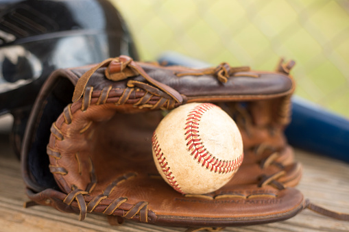 A close-up of a used dirty white softball in a leather glove sitting in the grass
