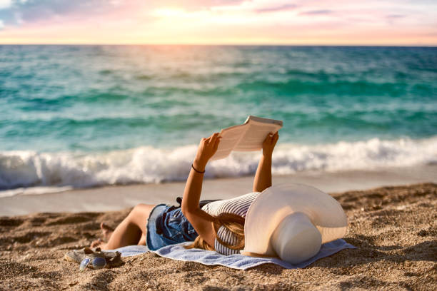 Young woman reads a book on the beach by the sea stock photo beautiful women,sunny,looking,shiny,vitality,photography,Serbia,horizontal,fashion,heat-temperature,human body part,hat,20-29 years,30-39 years,on the move,multi colored,motion,sun,Caucasian ethnicity, kindle and ook stock pictures, royalty-free photos & images