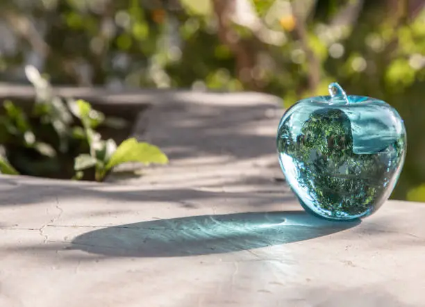 Glass/Crystal blue apple and reflective surface on a natural green background. Copy space, Selective focus.