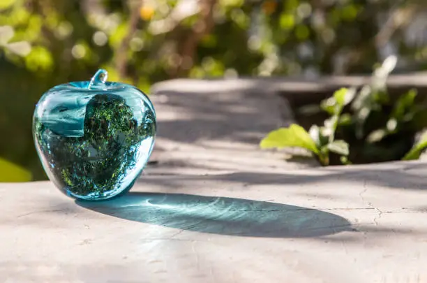 Glass/Crystal blue apple and reflective surface on a natural green background. Copy space, Focus and blur.