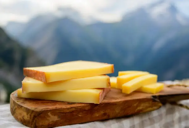 Cheese collection, French comte, beaufort or abondance cow milk cheese served outdoor with Alps mountains peaks in summer on background