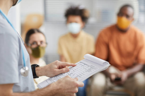 Male Nurse Checking Vaccination Chart Close up of male doctor holding clipboard while talking to patients waiting in line at medical clinic, copy space covid 19 patient stock pictures, royalty-free photos & images