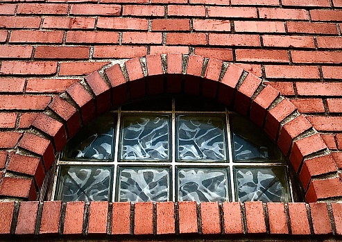 An arched block glass transom window adds architectural interest  to a red brick building in Hoboken, New Jersey.
