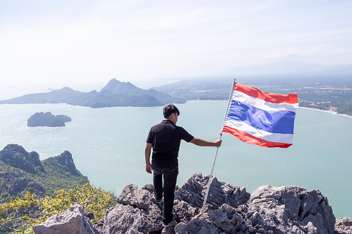 Men in black are standing on top of the mountain and are holding the Thai flag in Prachuap Khiri Khan province. Thailand.  The adventure is done.