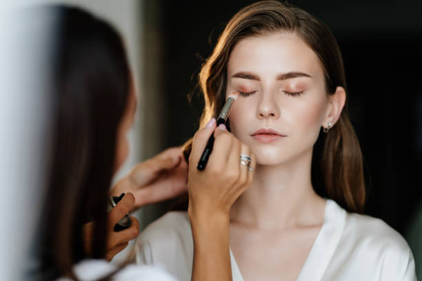 una hermosa joven con el pelo largo haciendo maquillaje para una boda o sesión de fotos - ceremonial makeup fotografías e imágenes de stock