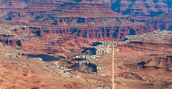 A straight gravel road takes people down to the floor of the beautiful landscape of Canyonlands National Park in Utah, USA.