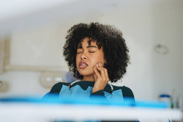 She's come to the right place for that tooth pain Shot of a young woman suffering from toothache while sitting in the dentist’s chair toothache stock pictures, royalty-free photos & images