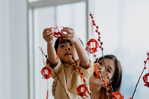 giovane ragazzo asiatico cinese che aiuta la madre ad appendere la decorazione del capodanno cinese - malaysian person family asian ethnicity mother foto e immagini stock