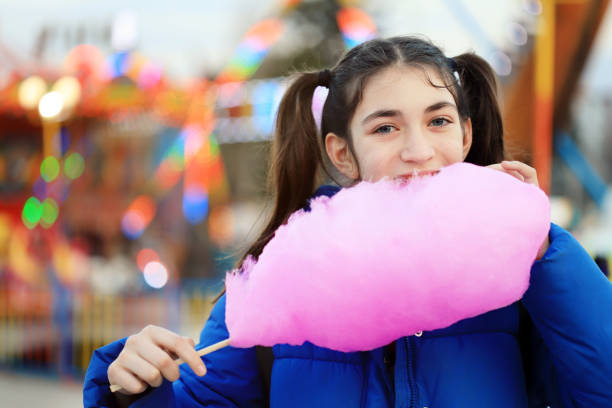 Girl eating cotton candy in amusement park Happy young girl cotton candy in amusement park child cotton candy stock pictures, royalty-free photos & images