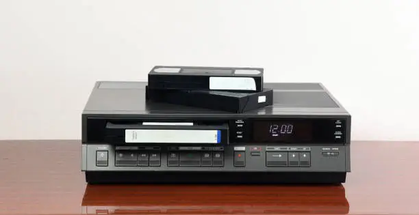 Photo of An old vintage videotape recorder from the 1980s stands on a dark table with a videotape. Retro VCR.