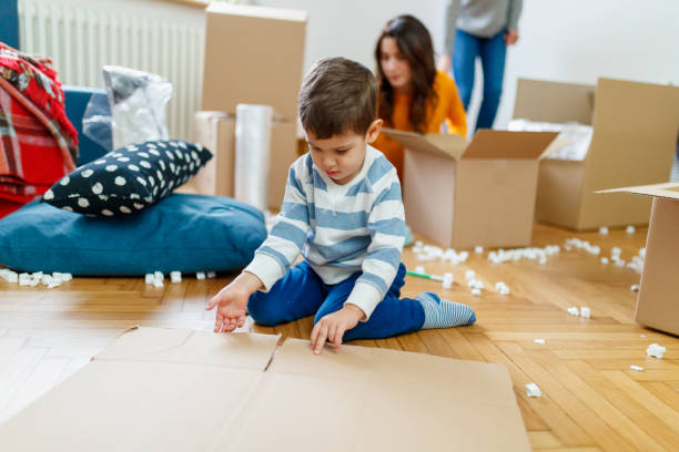 istock Toddler w-sitting on messy floor, picking up folded cardboard box during house move 1296452936