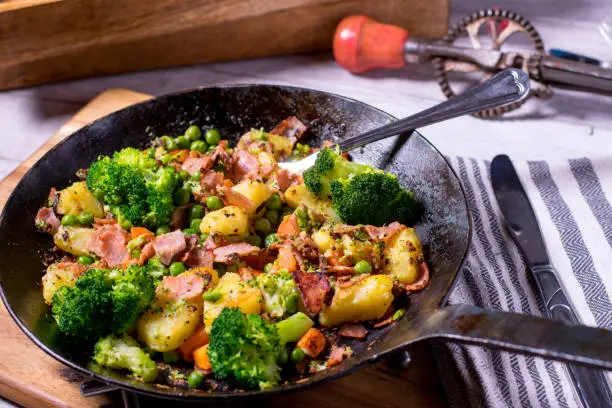 low fat meal with pan fried potatoes, vegetables and crispy ham in a cast iron pan