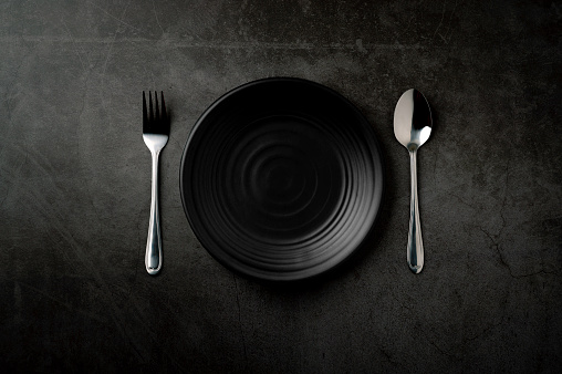 Empty plates, spoons and forks Black kitchen utensils set on a stone table. Flat top view with copy space.