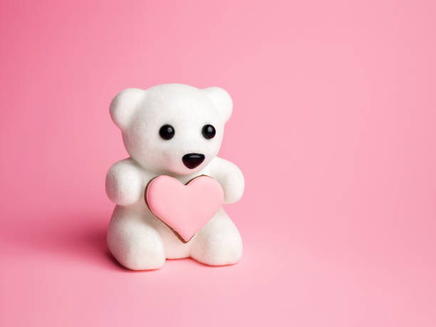 istock White teddy bear holding a heart shaped cookie on pink background 1296458088