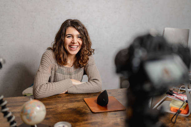 istock Young smiling woman sitting at the desk talking to the camera while recording a tutorial video. 1296462488