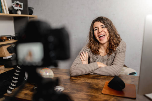 istock Young smiling woman sitting at the desk talking to the camera while recording a tutorial video. 1296462584