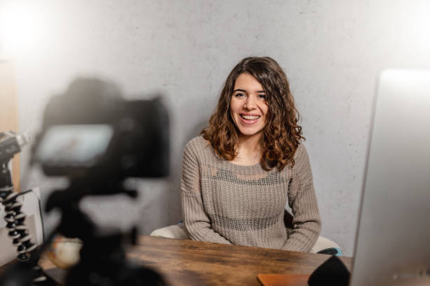istock Young smiling woman sitting at the desk talking to the camera while recording a tutorial video. 1296462619
