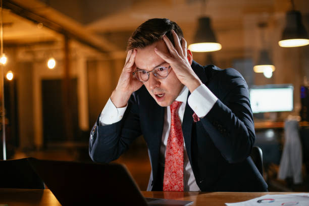 istock Tired man sitting at office desk working on laptop computer 1296465151