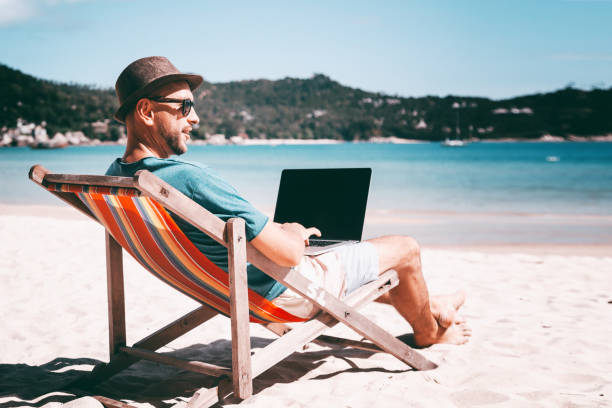 istock Attractive young man with laptop working on the beach. Freedom, remote work, freelancer, technology, internet, travel and vacation concepts 1296465895