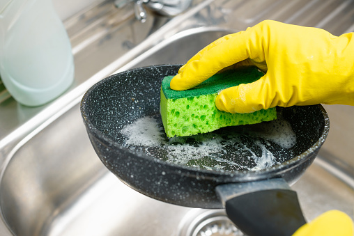 Hand with a sponge washes a dirty frying pan under running water.