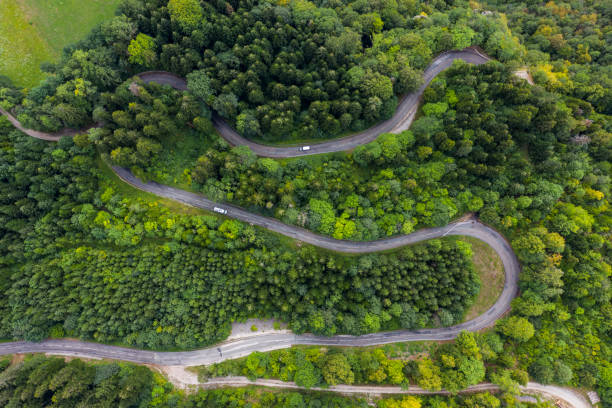 Aerial view of a winding countryside road passing through the green forest and mountain. White camping cars are passing through. Aerial view of a winding countryside road passing through the green forest and mountain. White camping cars are passing through. jura france stock pictures, royalty-free photos & images