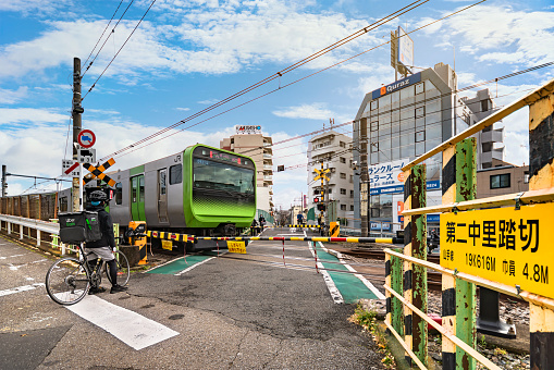 tokyo, japan - december 06 2020: Japanese Uber Eats delivery boy on a bicycle waiting that a Japan Railway train passing over the level crossing of Yamanote line called Nakazato railroad crossing II.