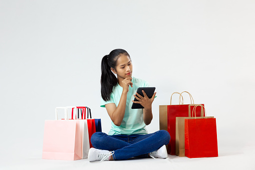 Asian woman black hair with colorful shopping paper bags, hold tablet shopping online posing on the white background.