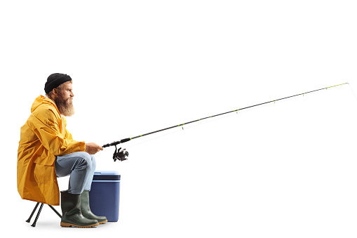 Profile shot of a bearded fisherman catching with a fishing pole seated on a chair isolated on white background