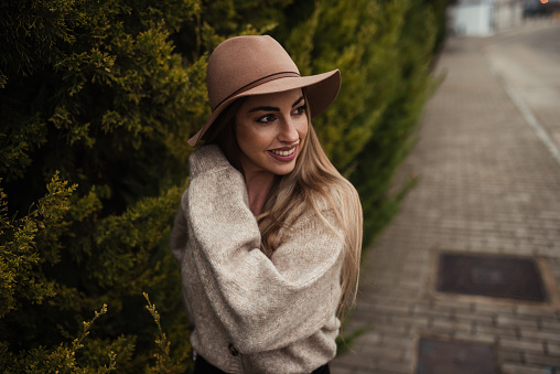 An outdoors portrait with autumn tones of a young woman wearing a brown sweater and a hat