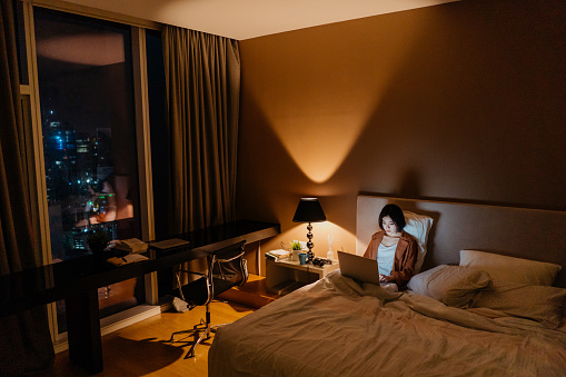 Image of an Asian Chinese woman using laptop and working late in bed
