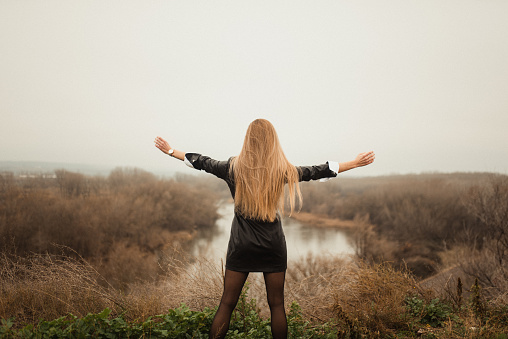 Rear view of a young woman with arms raised by a river on a foggy day