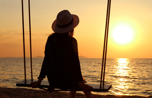Silhouette of a woman in hat relaxing on the swing at sunset, (Self Portrait)
