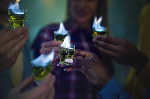 Close up of unrecognizable people holding burning shots of absinthe during a party.